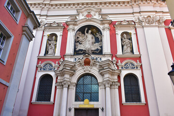 Facade of historic building with high windows, in white and pink colors. Decorated with statues, columns and decorative elements. Church facade. Poland, Poznan, July 2022