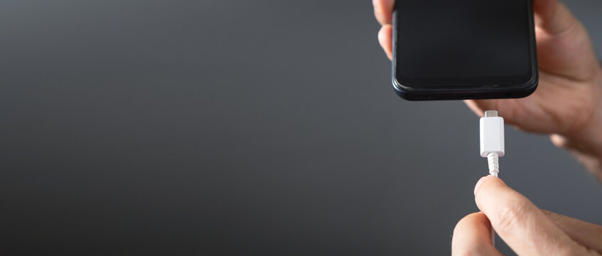 Man connecting charger cable to mobile phone.