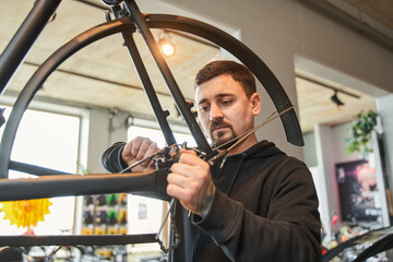 Fototapeta na wymiar Young caucasian repairman guy installing bike cassette on wheel in modern workshop