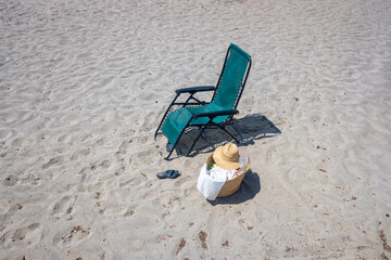 isolated lounger on the beach, sandals and a basket with beach items and a hat