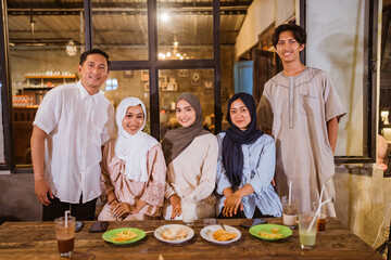 a group of Muslim friends smile at the camera while gathering to break their fast at an outdoor cafe