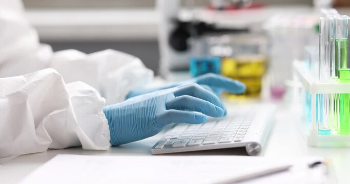 Scientist chemist in protective suit and gloves typing on keyboard near test tubes in laboratory 4k movie. Development of vaccine against covid19 concept