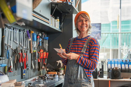 Positive craftswoman taking notes in the workshop while preparing repairing bicycles - Powered by Adobe