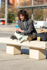 Woman commuter sitting on bench by the street using mobile phone