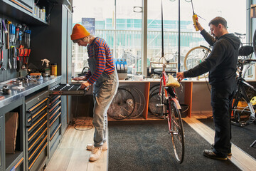 Full length view of the female bicycle mechanic taking details from box while repairing bicycles