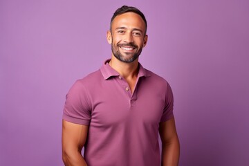 Portrait of a handsome young man smiling and looking at the camera while standing against purple...