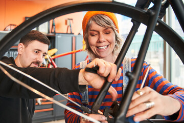Two smiling colleagues repairing bicycle in workshop