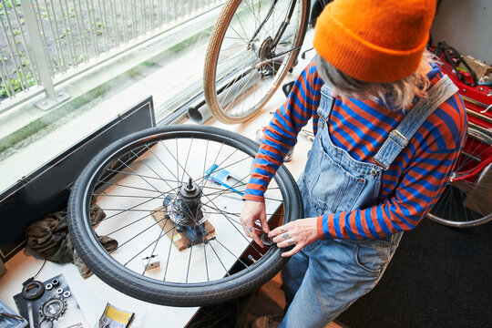 Beautiful adult female mechanic enjoying while repairing bicycle wheel in a workshop