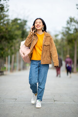 Full body portrait smiling young woman walking with mobile phone and bag