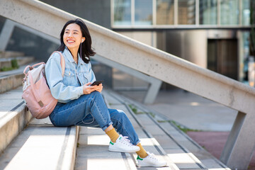 smiling young asian woman sitting with mobile phone outside