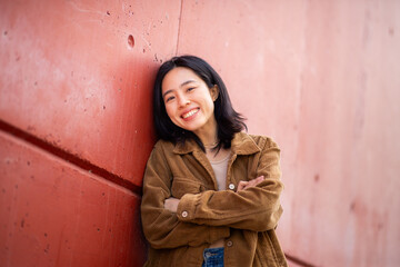 happy young asian woman with arms crossed leaning against wall