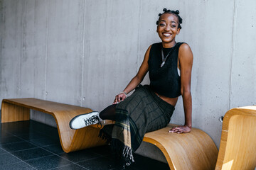 Positive african woman smiling sitting on bench in art gallery. Black woman enjoying spending time...