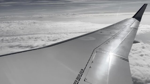 wing of an airplane in the air with a blue background with clouds. 4k black and white video.