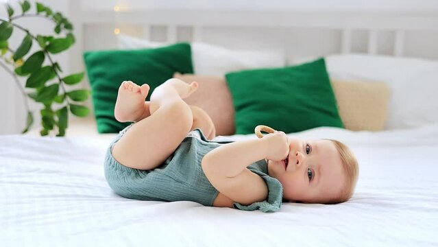 little baby girl lying on the back of the bed at home biting a rodent toy, cute funny baby at home playing and smiling, lifestyle, teething