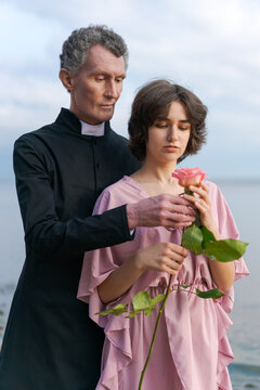 a young woman in a pink dress and an elderly man stand together on the seashore at sunset. the concept of the relationship of different ages in a couple