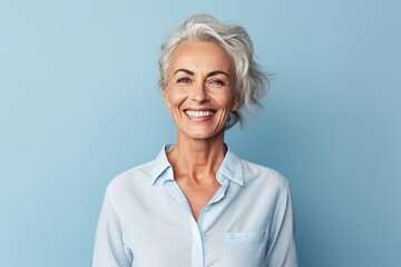Portrait of happy senior woman looking at camera and smiling while standing against blue background - Powered by Adobe
