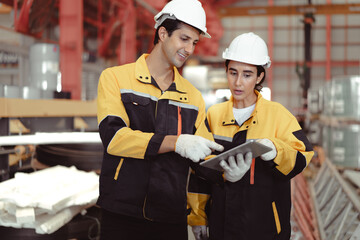 Latino industrial engineer in white helmet and safety jacket work in heavy metal engineering factory. Technician worker team using tablet computer control metalwork in manufacturing facility, portrait