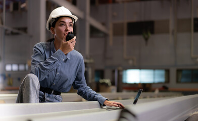 Factory female worker using laptop computer checking, talking to supervisor in heavy metal production facility. Woman technician in white hardhat working, inspecting quality control in manufacturing.