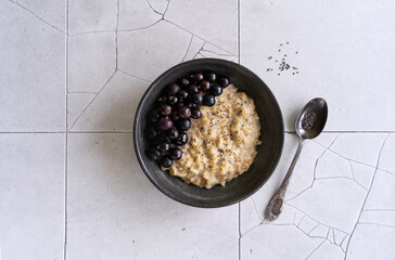 Oatmeal porridge with fresh black currant berries and chia seeds for breakfast. Healthy breakfast with superfood. Taking care of your health. A bowl of food stands on a ceramic table.