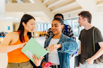 Asian student and Latina student chat and check facts about their studies in their university notes...