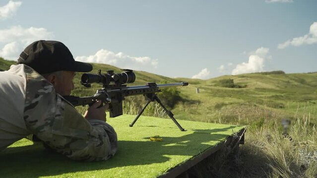 A shooter in a black cap reloads a sniper rifle and shoots at the target