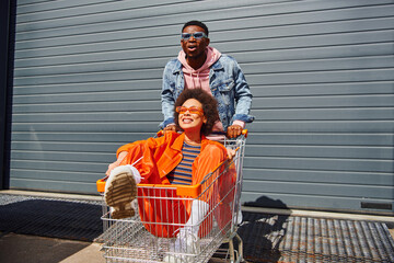 Excited young african american man in sunglasses and denim jacket standing near smiling best friend...