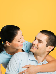 Fototapeta premium Smiling happy amazed couple. Portrait of standing close and looking at each other models in love studio concept, isolated over yellow background. Young man and woman posing together. Copy space.