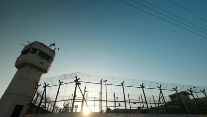An extreme wide angle of prison and a watchtower, the last sun rays are penetrating through the fence, minutes before sundown. - Powered by Adobe