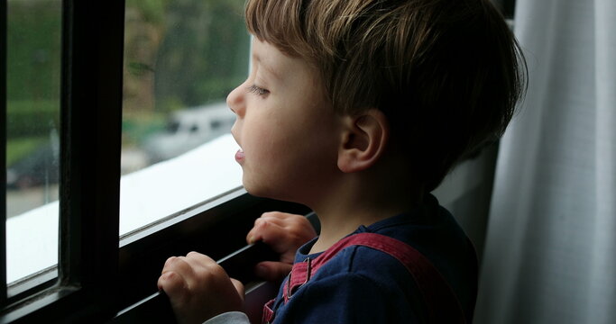 Kid Standing By Window Looking Outside Child Stares Out Leaning On Window