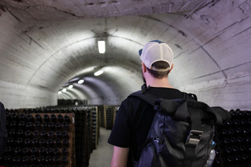 Back view a tourist with a backpack stands at the production of champagne. Looking at botle rack during champagne production during a tour in the basement. Rimming. Tourist tour. Champagne production