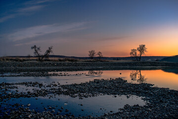 A river with a mirror surface at dusk. Sunset over a river with a pebbly shore.