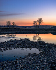 Naklejka premium A river with a mirror surface at dusk. Sunset over a river with a pebbly shore.