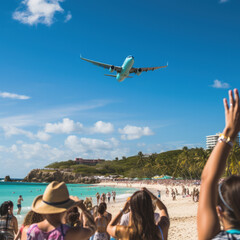 A plane flying over island beach with people looking up by the turquoise blue ocean sea