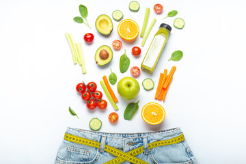 Fresh fruit, vegetables, smoothie falling into jeans and yellow measuring tape as a belt on white background. Concept of healthy food for weight loss, detox, diet, healthy clean nutrition