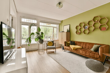 a living room with green walls and wood flooring the room has a brown leather couch, two chairs, a flat screen tv
