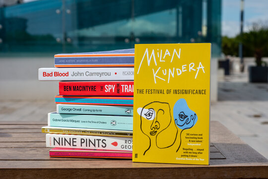 Close up Milan Kundera's The Festival of Insignificance novel on the wooden table. Stack of books.
