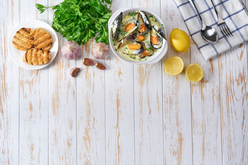 Chowder - delicious fish soup with mussels in a bowl on white wooden table.