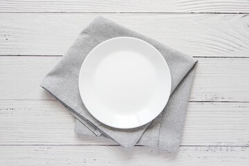 Empty white plate on grey napkin, top view, minimalist style composition on white wooden table, for...