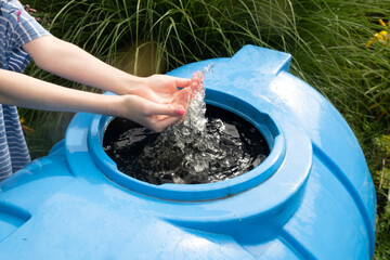 Faceless girl washes her hands in a barrel of rainwater. Rain water harvesting architecture