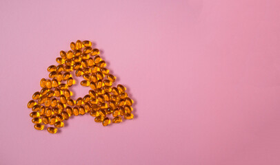 A shaped golden capsules vitamins omega fish oil close up medical concept pink background