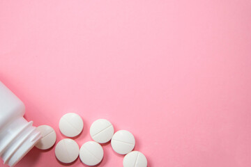 White pills spilling from plastic bottle on pink background. Minimal medical banner with copy...