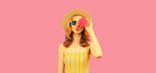 Summer portrait of stylish young woman model covering her eyes with flower buds as binoculars looking for something wearing round straw hat on pink background