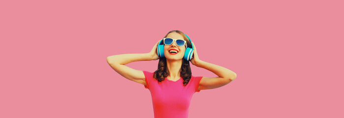 Obraz na płótnie Canvas Portrait of happy smiling young woman in wireless headphones listening to music on pink background