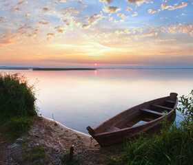 Sunset with old flooding boat on summer lake shore