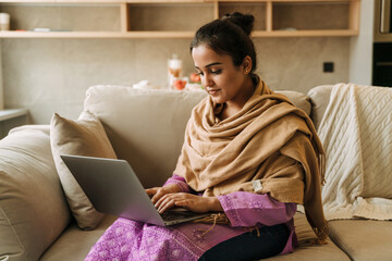 Young indian woman working with laptop while sitting on couch