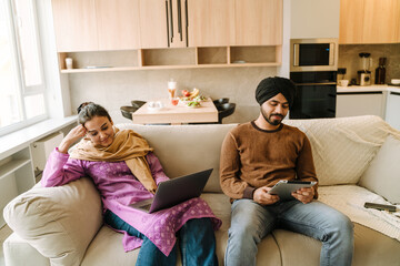 Indian couple sitting on sofa with laptop and tablet