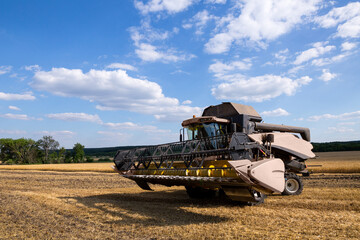 A modern combine harvester stands on the field during harvesting withe the hinged frame cutterbar draper combine header.