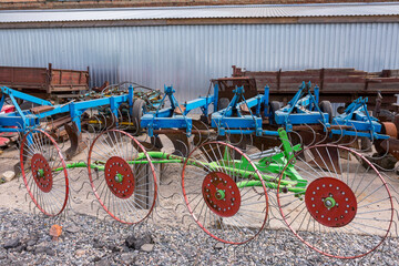 Fototapeta na wymiar Old trailed plough for tillage are standing near the arches hangar on the material and technical base of the agricultural enterprise. Farm enterprise in central region of Ukraine.