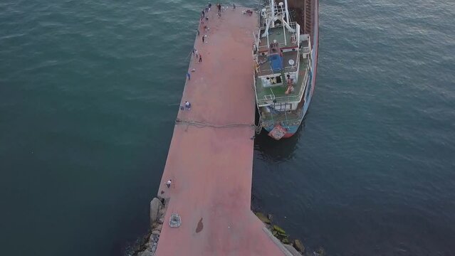 Fishermen reeling in fish on the pier and ship wreck. Fly over shot
