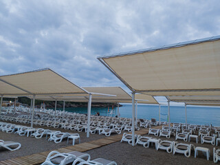 Rows of sunbeds and white sunshades at the sea at a beach resort in the evening time. Travel and...